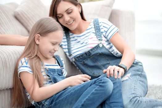 Mother with a little daughter using a smartphone sitting in the new living room.people and technology