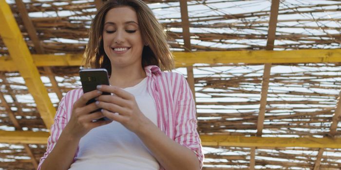 young woman using mobile cell smart phone app at beach during sunset on autumn day