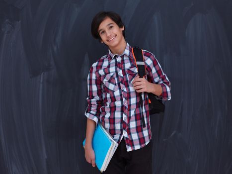 arab teenager with backpack and books wearing  casual western school look against black chalkboard background