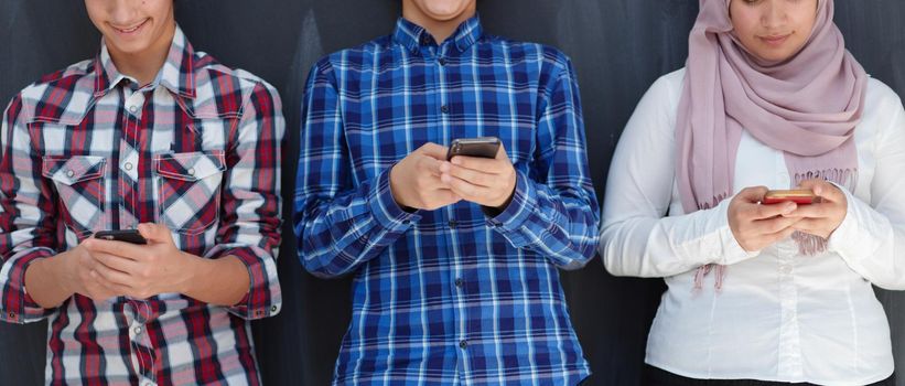 arab teenagers group using smart phones for social media networking against black chalkboard