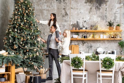 Merry Christmas and happy Holidays. Mom, dad and daughter decorating christmas tree