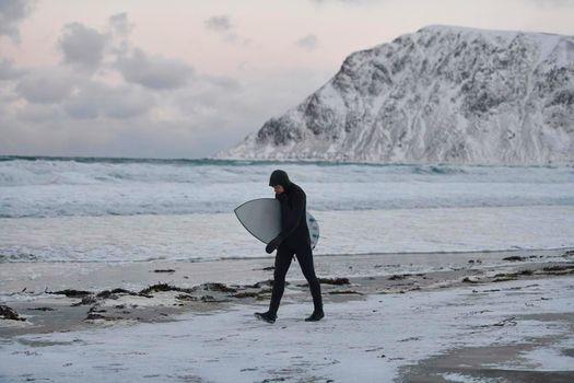Authentic local Arctic surfer going by beach after surfing in Northern sea. Norwegian sea coastline. Winter water activities extreme sport