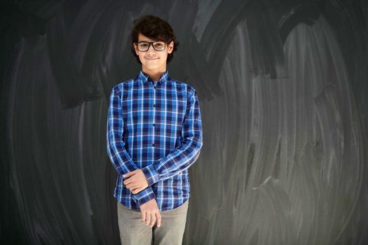 portrait  of smart looking arab teenager with glasses wearing a hat in casual school look against black chalkboard background