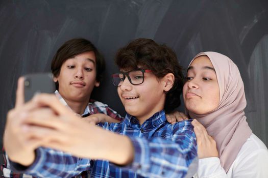 group of arab teens taking selfie photo on smart phone with black chalkboard in background