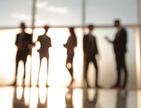 Silhouettes of businesspeople standing against panoramic office window