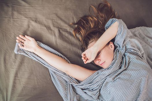 Beautiful young woman lying down in bed and sleeping, top view. Do not get enough sleep concept.