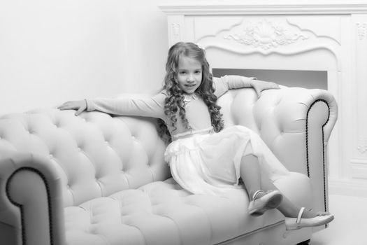 Little girl is sitting on the couch in the room. The concept of a happy childhood.