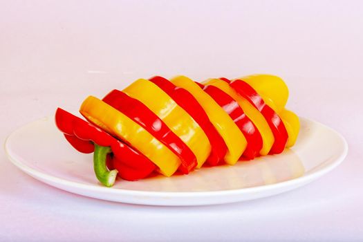 Bulgarian pepper red and sliced yellow lies on a white plate. The concept of a healthy diet.