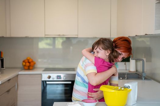 Funny little baby helper playing with dough on his hands learning to knead helps adult mom in the kitchen, happy cute baby daughter and parent mom have fun cooking cookies. High quality photo