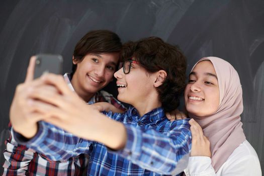 group of arab teens taking selfie photo on smart phone with black chalkboard in background