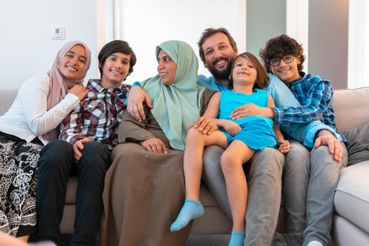 Portrait photo of an Arab Muslim family sitting on a couch in the living room of a large modern house. Selective focus. High quality photo