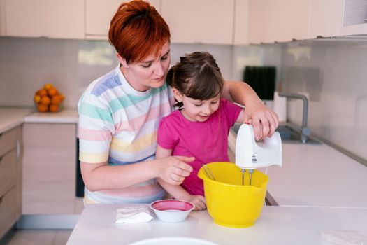 Funny little baby helper playing with dough on his hands learning to knead helps adult mom in the kitchen, happy cute baby daughter and parent mom have fun cooking cookies. High quality photo