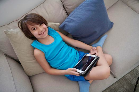 Little Arabian boy sitting on sofa and playing game on digital tablet. Portrait of a young arab child at home watching cartoon on the laptop. Modern kid and online education elearning technology.