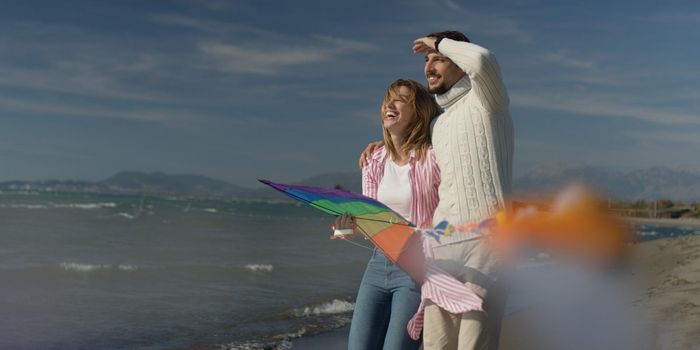 Loving Couple Flying A Kite at Beach and having fun on autumn day