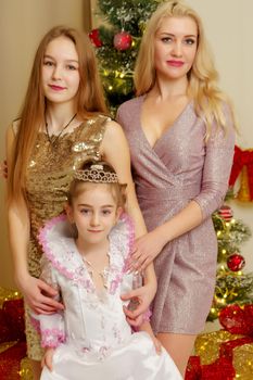Happy mother with two daughters on Christmas Eve, near the New Year tree. Family holidays concept.