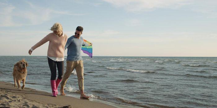 Couple Running On The Beach Holding Their Hands with dog On autmun day