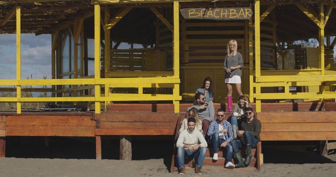 Happy Group Of Friends Hanging Out At Beach House having fun and drinking beer on autumn day