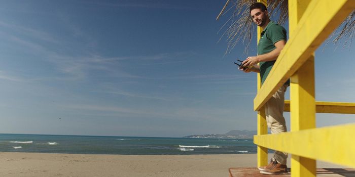 Man operating drone with remote controler by the sea on autumn day