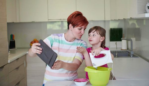 Happy family in the kitchen playing games and learning to cooking while staying at home during coronavirus covid-19 pandemic isolation. Mother and child daughter preparing the cake and cookies.