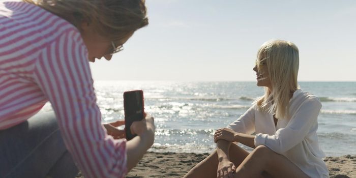 Two Girl Friends Taking Photo with Smartphone On Empty Beach during autumn day