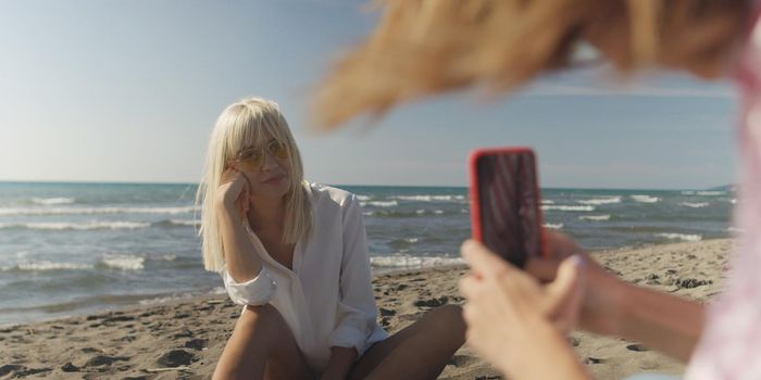 Two Girl Friends Taking Photo with Smartphone On Empty Beach during autumn day