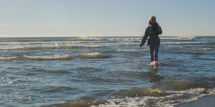 Young woman on the beach. The girl enjoying the warm autumn day. Portrait of beautiful girl near the water