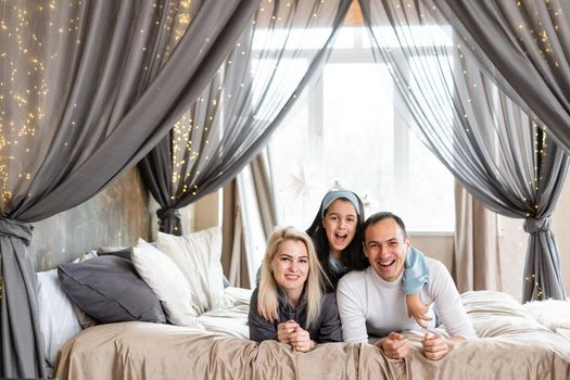 Top view of beautiful young mother, father and their daughter smiling while lying on bed.