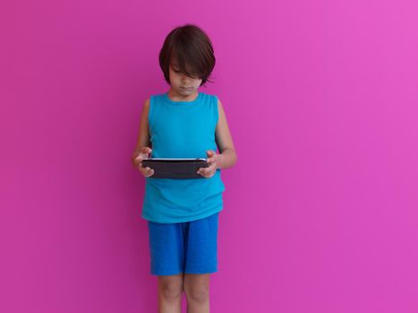 Little Arabian boy sitting using  on digital tablet. Portrait of a young arab child at home watching cartoon with pink background . Modern kid and online education elearning technology.