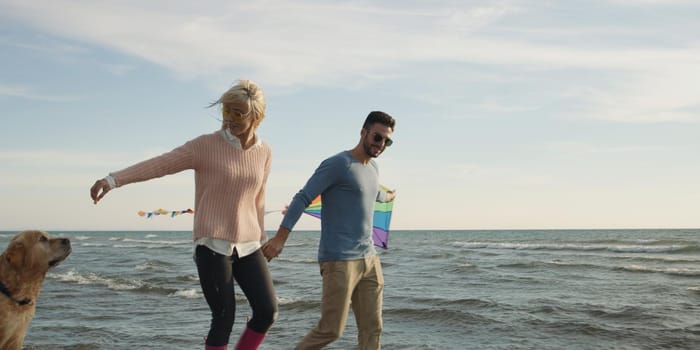 Couple Running On The Beach Holding Their Hands with dog On autmun day