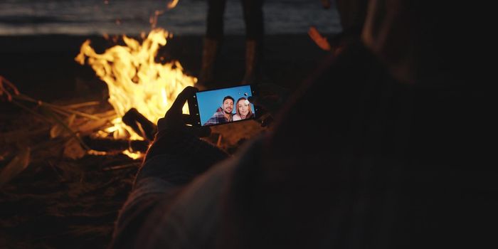 Boy Shows Girl A Picture On His Phone beside campfire on beach