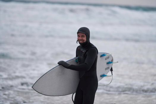 Authentic local Arctic surfer going by beach after surfing in Northern sea. Norwegian sea coastline. Winter water activities extreme sport