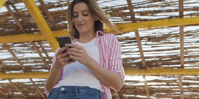 young woman using mobile cell smart phone app at beach during sunset on autumn day