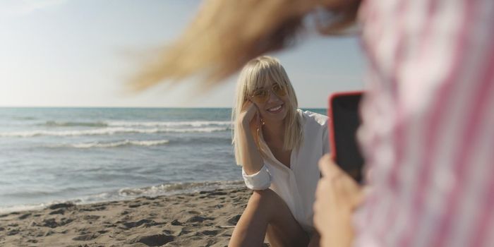 Two Girl Friends Taking Photo with Smartphone On Empty Beach during autumn day