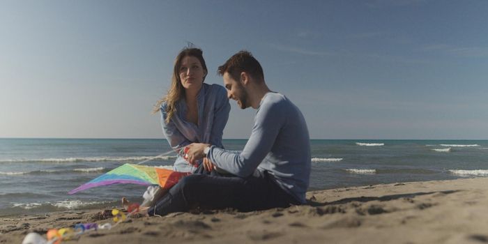 Young Couple having fun and Playing With A Kite On The Beach at autumn day