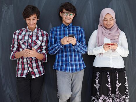 arab teenagers group using smart phones for social media networking against black chalkboard