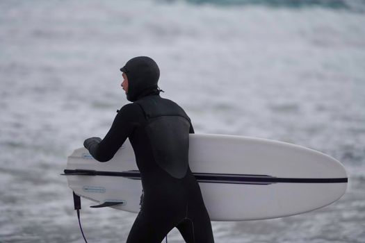 Authentic local Arctic surfer going by beach after surfing in Northern sea. Norwegian sea coastline. Winter water activities extreme sport