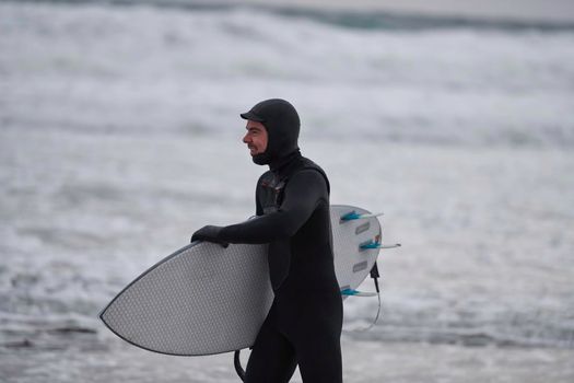 Authentic local Arctic surfer going by beach after surfing in Northern sea. Norwegian sea coastline. Winter water activities extreme sport