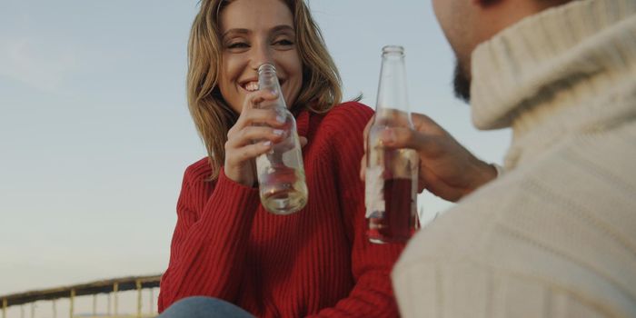 Young Couple Relaxing By The Fire, Drinking A Beer Or A Drink From The Bottle.