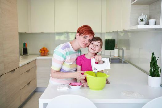 Happy family in the kitchen playing games and learning to cooking while staying at home during coronavirus covid-19 pandemic isolation. Mother and child daughter preparing the cake and cookies.