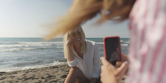 Two Girl Friends Taking Photo with Smartphone On Empty Beach during autumn day