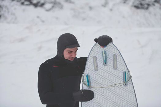 Authentic local Arctic surfer portrait holding a board after surfing in Norwegian sea. Snow capped mountain background. Winter water activities extreme sport