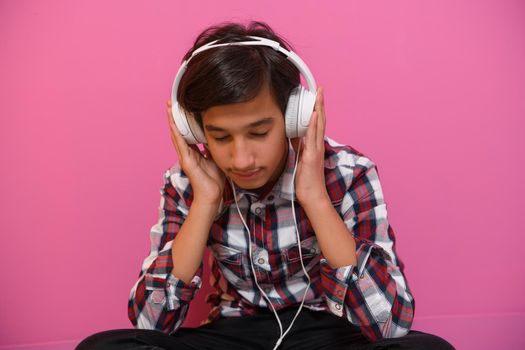 Arabic Teenage Boy Wearing Headphones And Listening To Music pink background. High quality photo