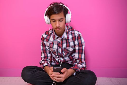 Arabic Teenage Boy Wearing Headphones And Listening To Music pink background. High quality photo