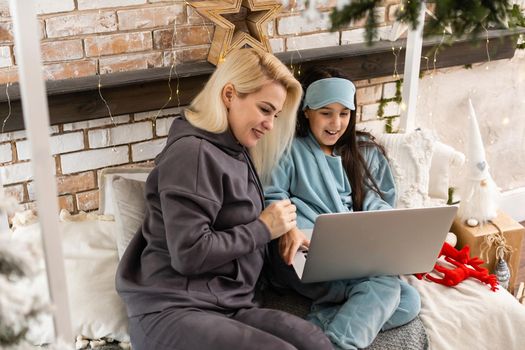 Caucasian woman with her daughter at christmas, having video chat with friends and family on laptop screen, sitting on sofa at home embracing. social distancing during covid 19 pandemic at christmas