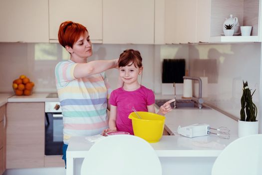 Funny little baby helper playing with dough on his hands learning to knead helps adult mom in the kitchen, happy cute baby daughter and parent mom have fun cooking cookies. High quality photo