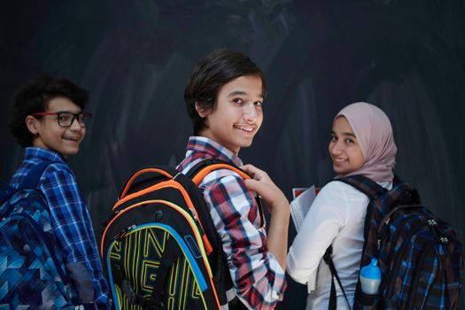 Arabic teenagers, students group  portrait against black chalkboard wearing backpack and books in school