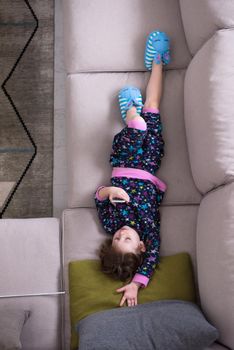 top view of cute little girl using a smartphone and smiling while lying on the sofa at home