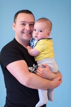 portrait of happy young father holding newborn baby boy isolated on a blue background