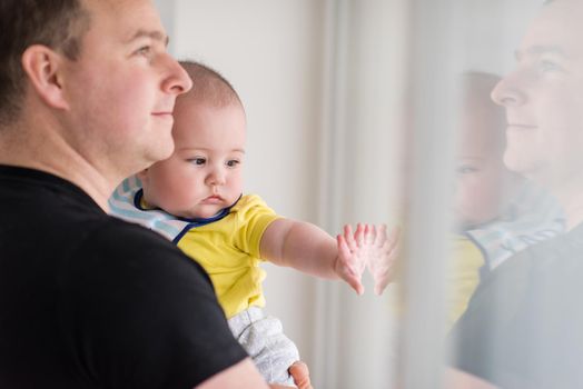 portrait of happy young father holding newborn baby boy near the window at home