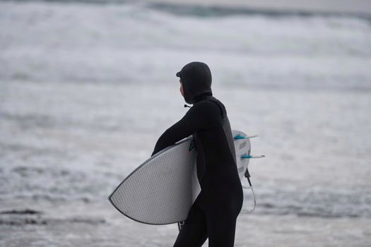 Authentic local Arctic surfer going by beach after surfing in Northern sea. Norwegian sea coastline. Winter water activities extreme sport